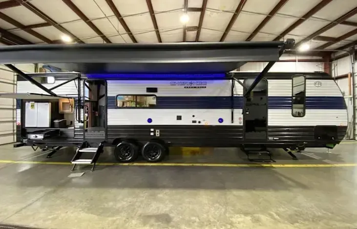 Blue and white travel trailer with awning extended, parked inside a building.