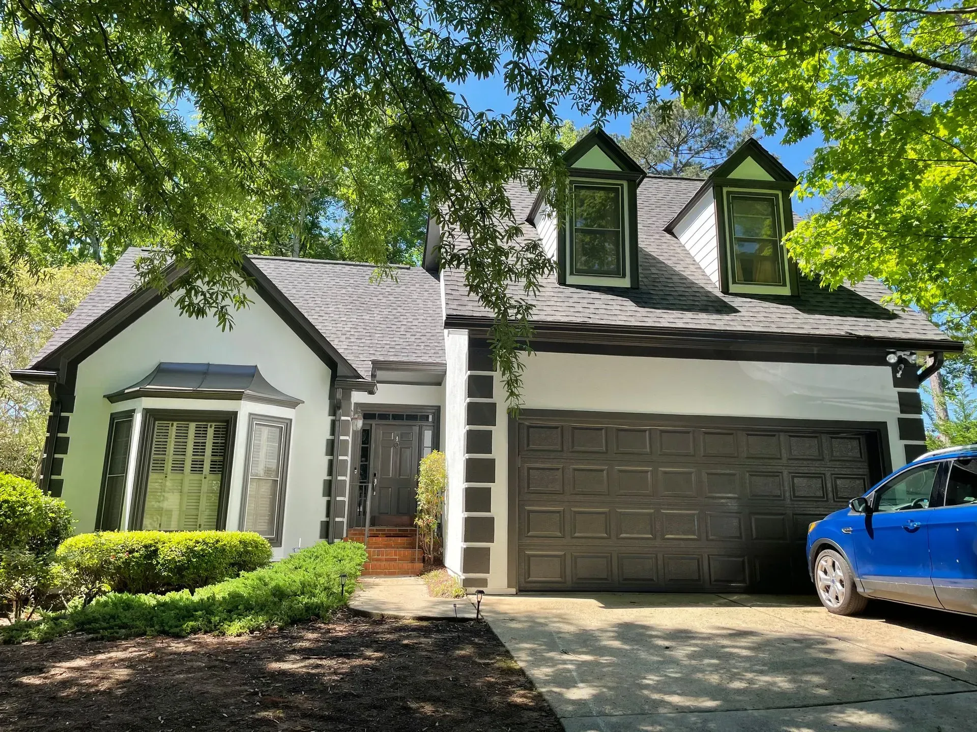 White house with black trim, dark gray garage door, blue car parked in front.