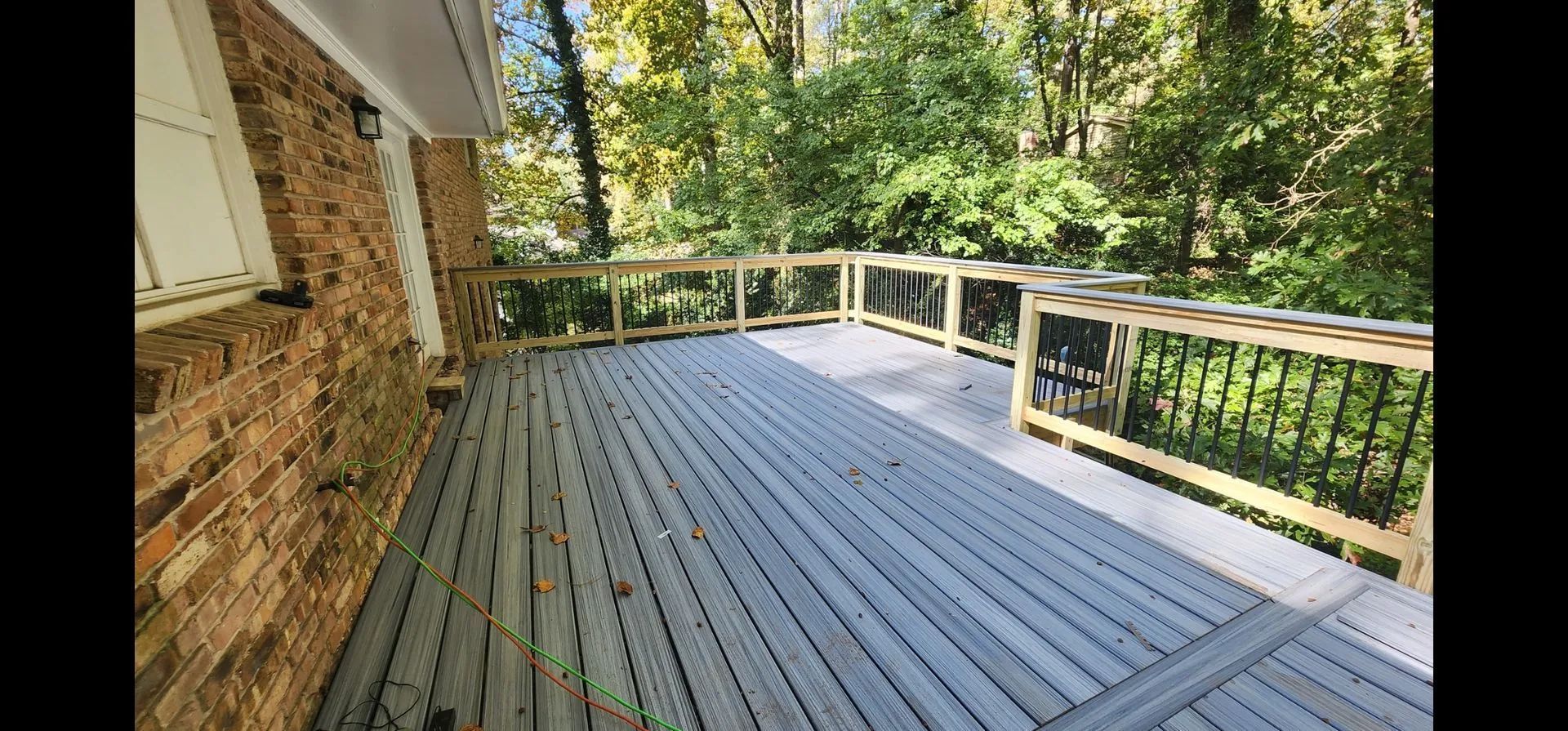 Wooden deck with gray planks, wooden railings, and greenery in the background.