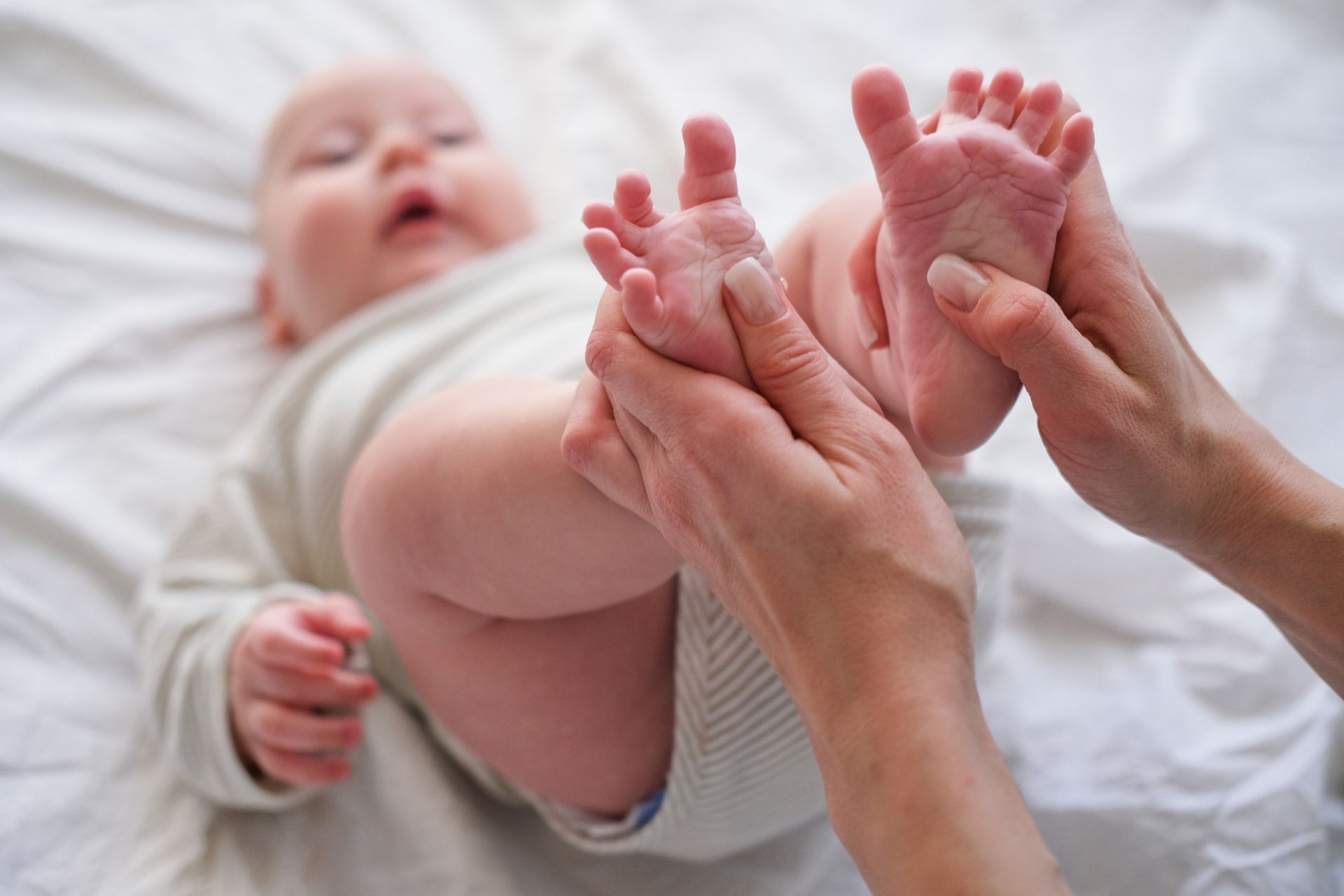 A woman is massaging a baby 's feet on a bed.