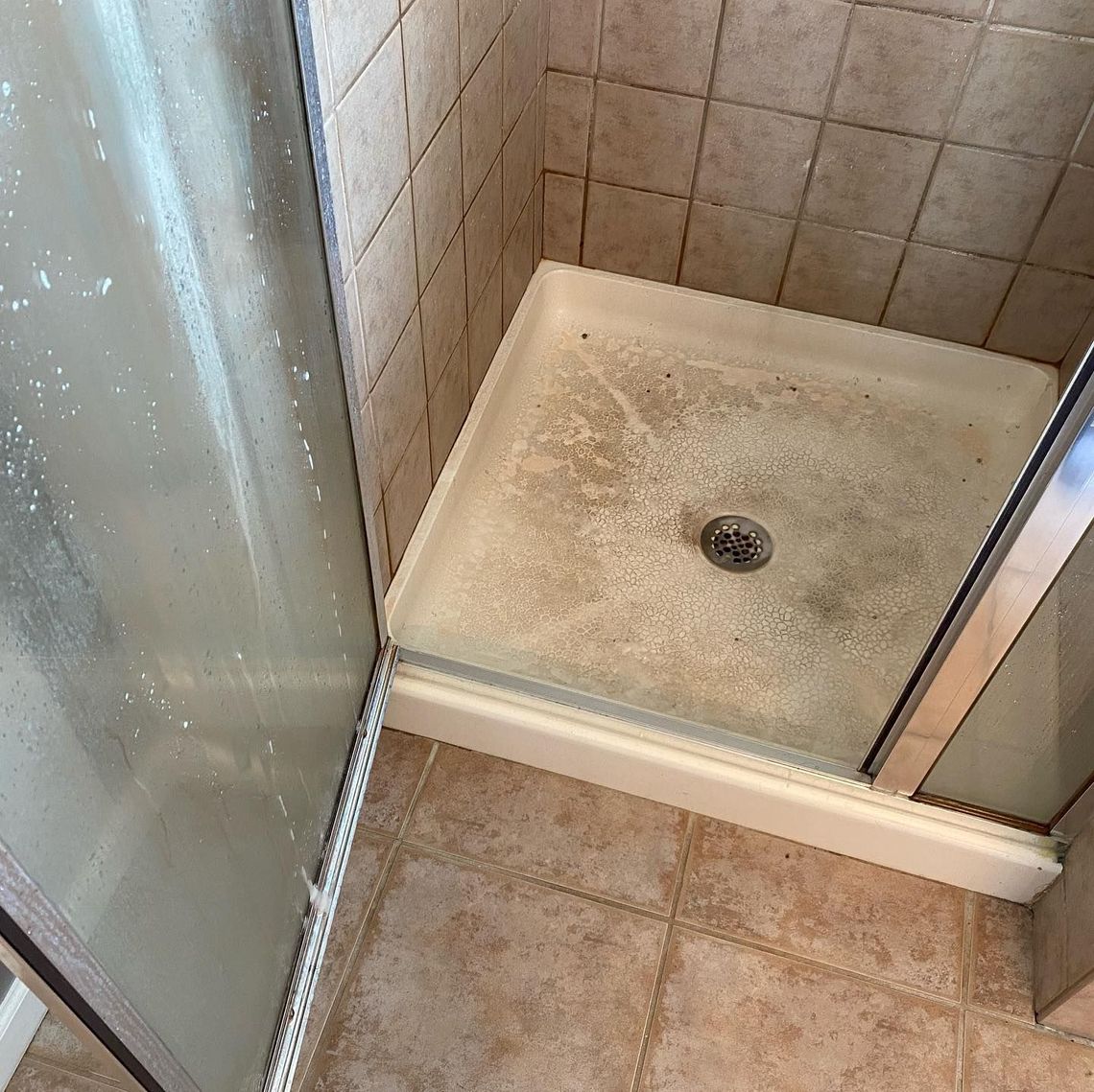A dirty shower stall in a bathroom with a drain.