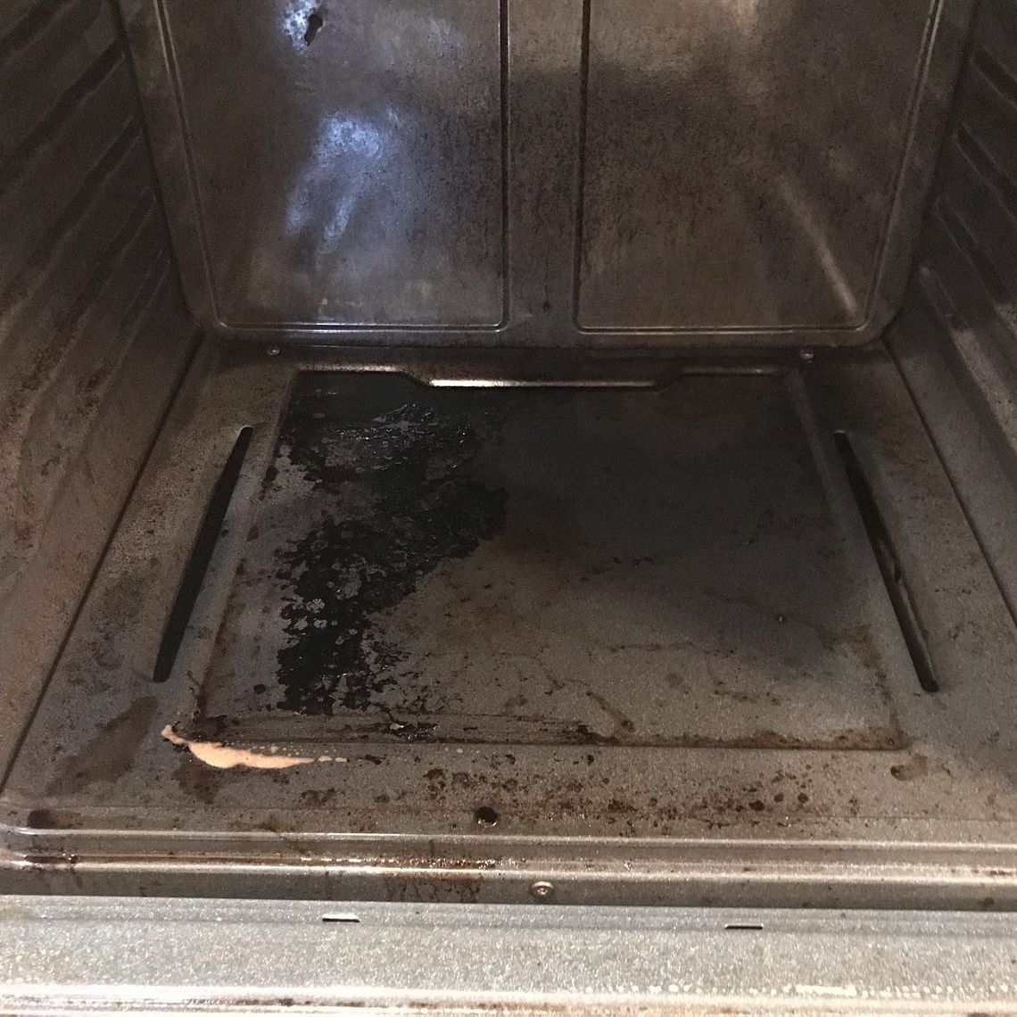 The inside of an oven with a dirty tray in it.