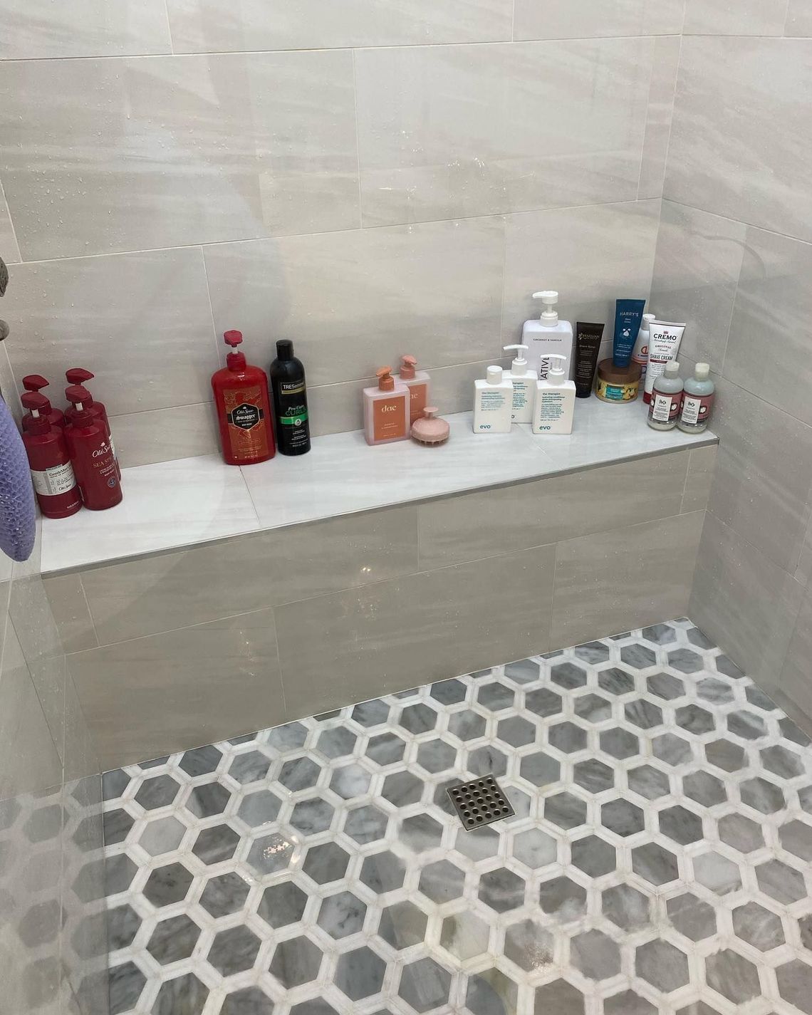 A shower with a shelf filled with bottles of shampoo and conditioner.