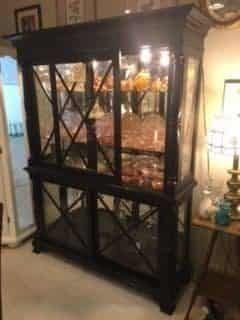 A large glass cabinet is sitting in a living room next to a table.