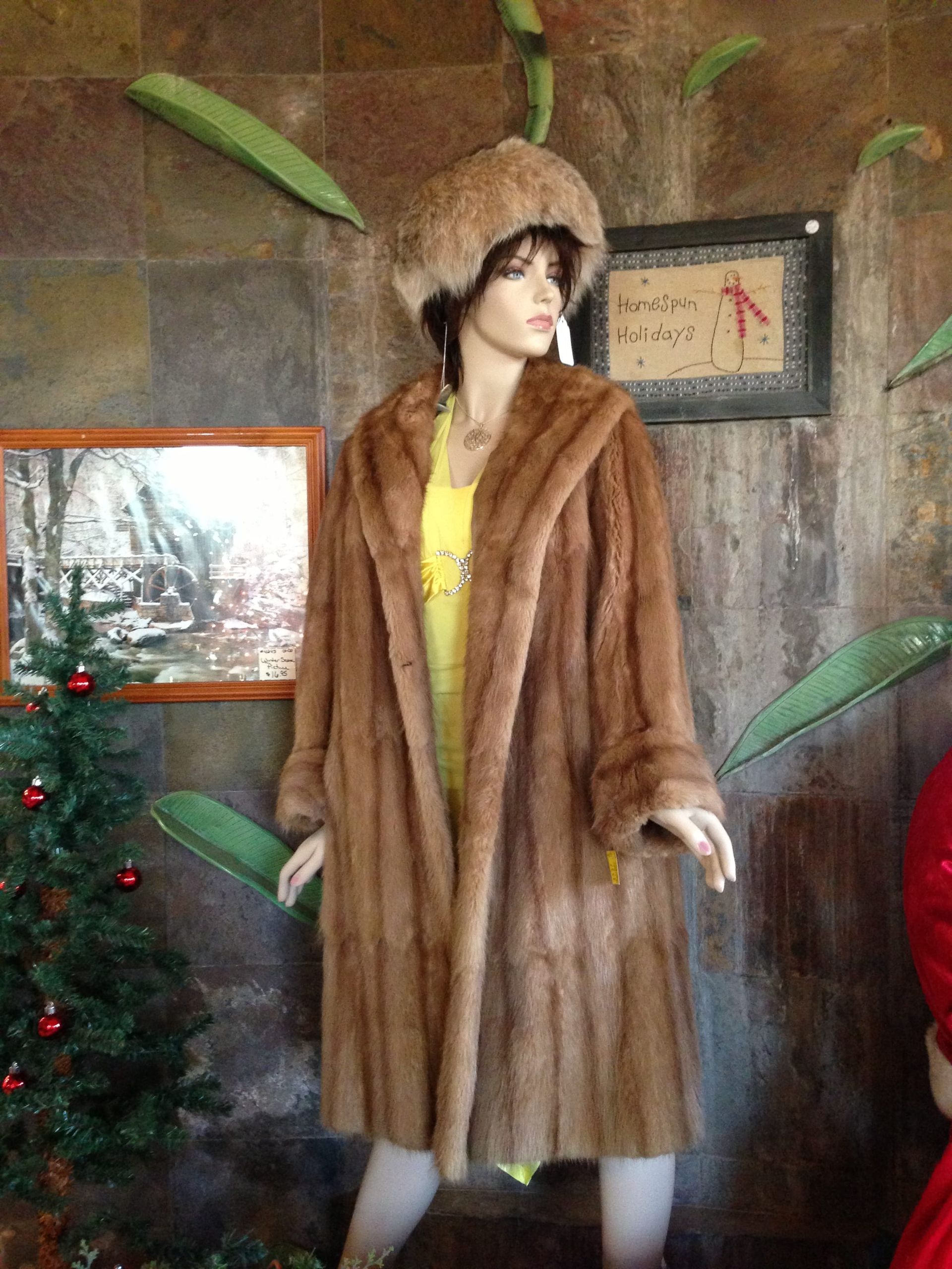 A mannequin wearing a fur coat and hat is standing in front of a christmas tree.