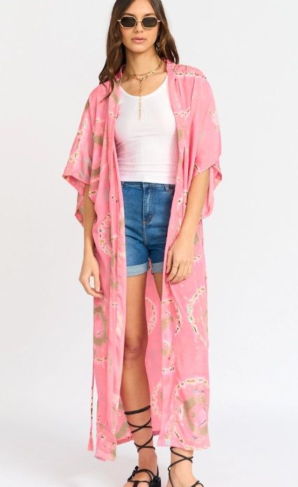 Mujer con kimono rosa estampado y sandalias. De pie sobre un fondo blanco.