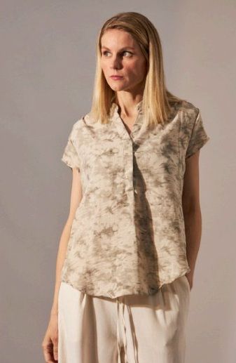 Mujer que lleva una blusa estampada en color beige con cuello en V y mangas cortas, combinada con pantalones de color crema.