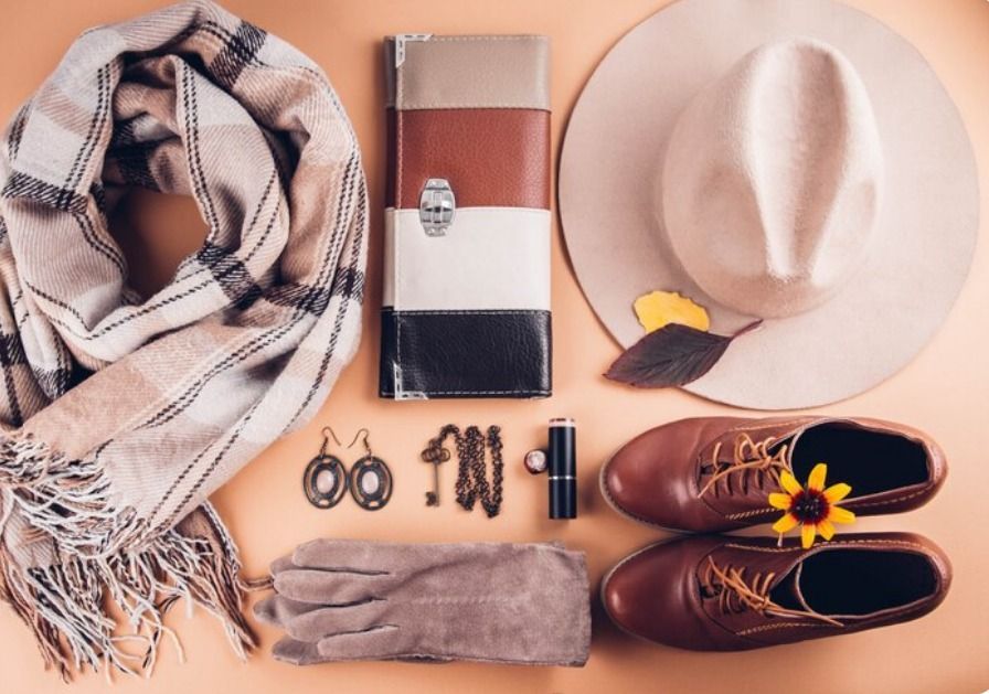 Plano de moda otoñal: bufanda, gorro, cartera, zapatos, joyas, guantes y pintalabios sobre una superficie de melocotón.