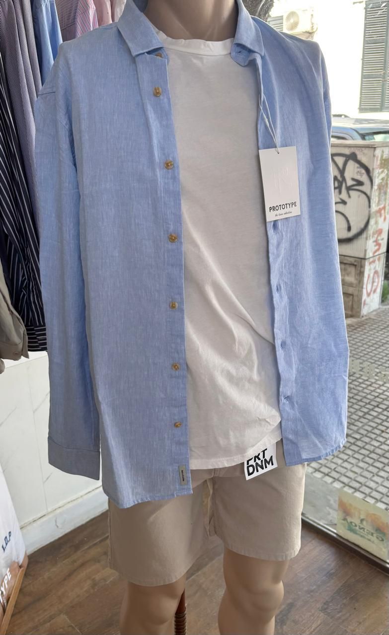 Maniquí con camisa azul, camiseta blanca y pantalón corto beige. Exhibido en una tienda.