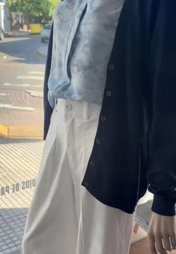 Pantalones anchos color crema con pliegues y blusa a juego. La persona está de pie en el interior.