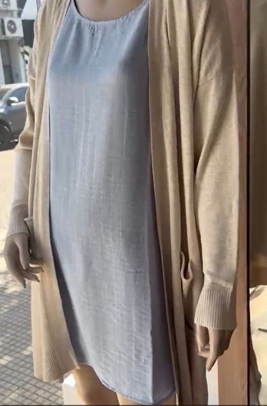 Mujer que lleva un vestido de lino azul sin mangas, de pie frente a un fondo blanco.