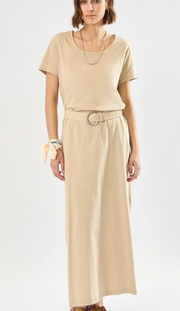 Mujer con vestido largo beige, sonriente, con cinturón y collar.