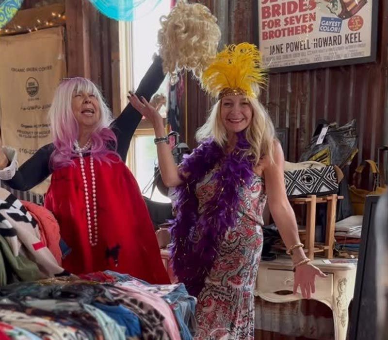 Two people in colorful costumes pose indoors, smiling and holding feather boas and pom-poms.