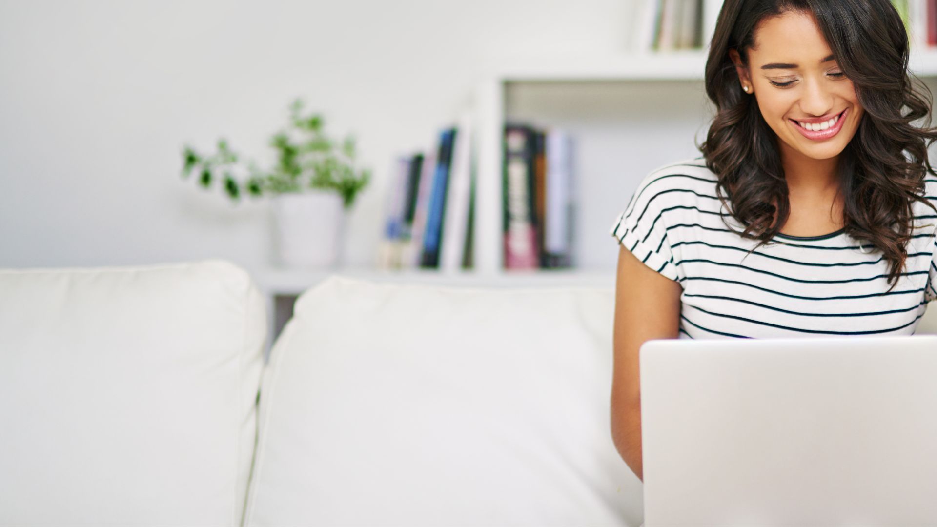 A woman is sitting on a couch using a laptop computer.