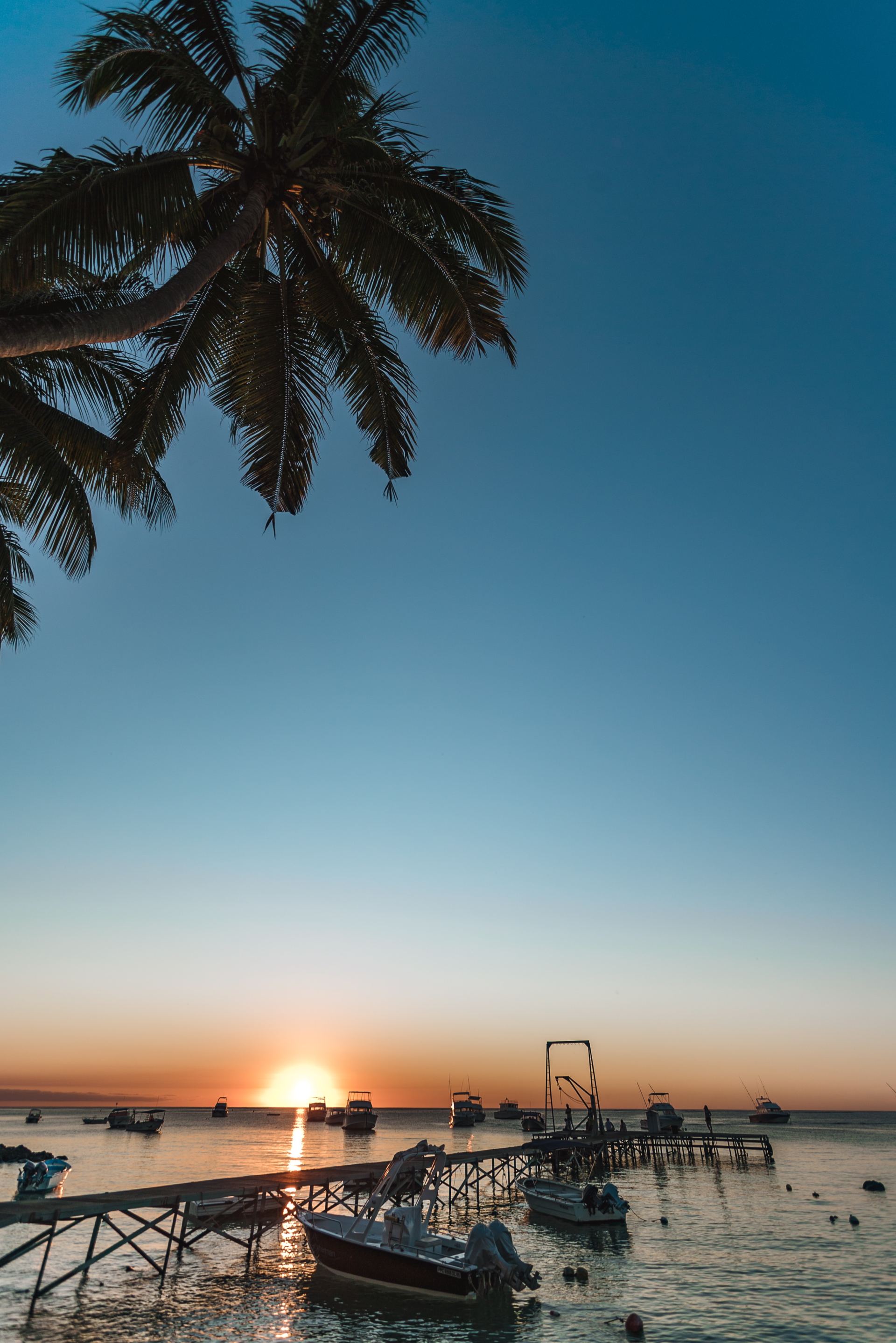 The sun is setting over the ocean with boats docked at a pier.