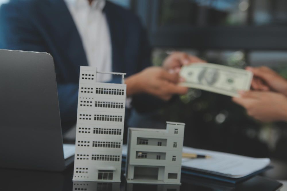 A man is giving money to another man in front of a model building.