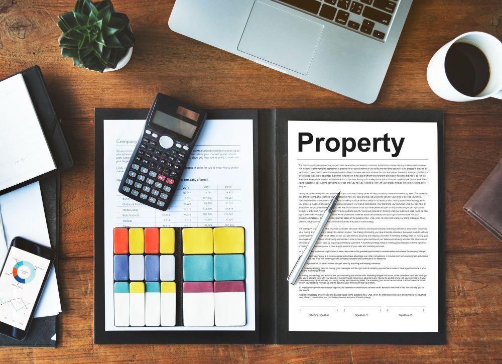A wooden desk with a laptop , calculator , cell phone , and a folder with the word property on it.