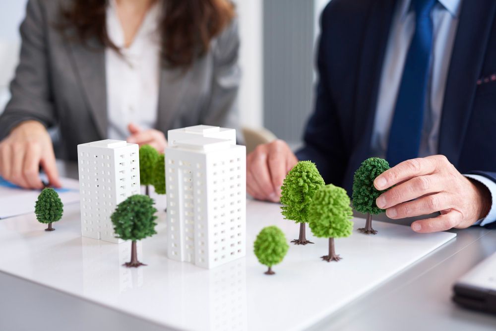 A man and a woman are sitting at a table with a model of buildings and trees.