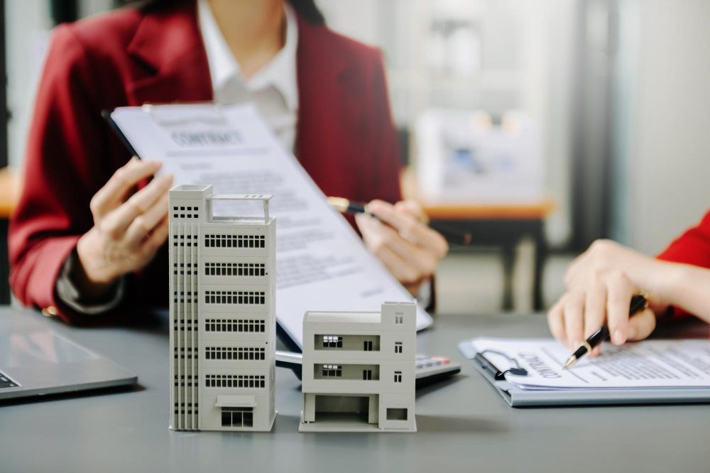 A woman is sitting at a table holding a piece of paper and a model of a building.