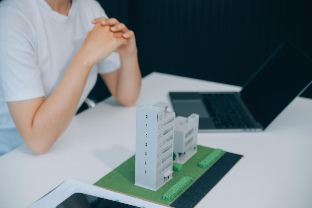 A woman is sitting at a table with a model of a building and a laptop.
