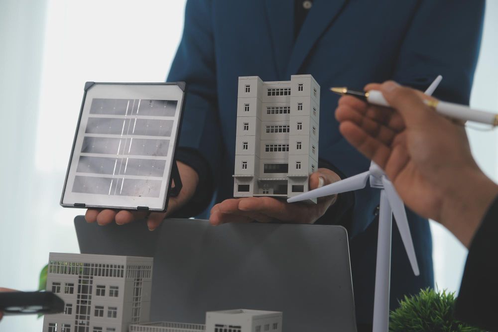 A man is holding a model of a building and a wind turbine.