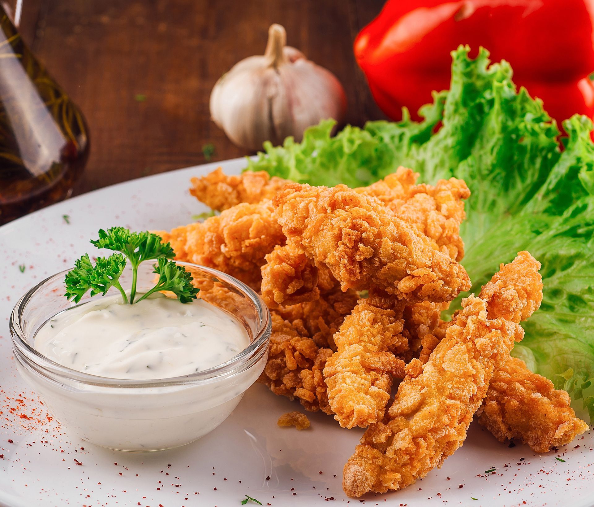 Fried chicken strips with dipping sauce, garnished with parsley, on a plate with lettuce.