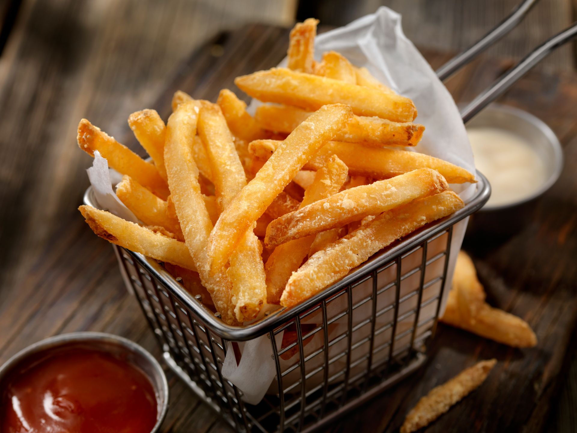 Basket of golden french fries with ketchup and dipping sauce.