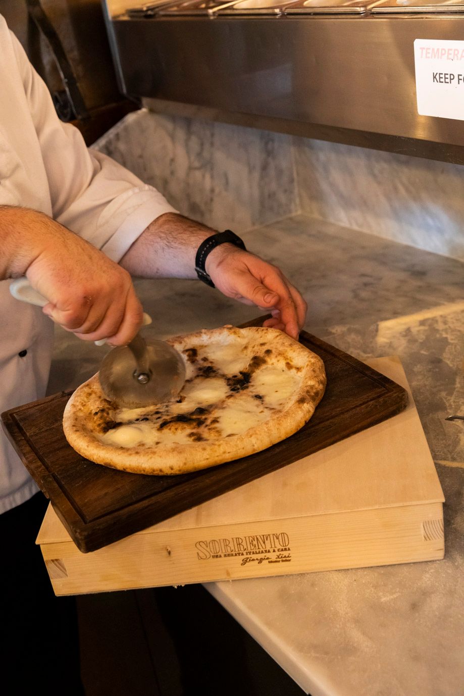 Chef cutting a cooked pizza on a wooden board, on a light wooden box, close-up view.