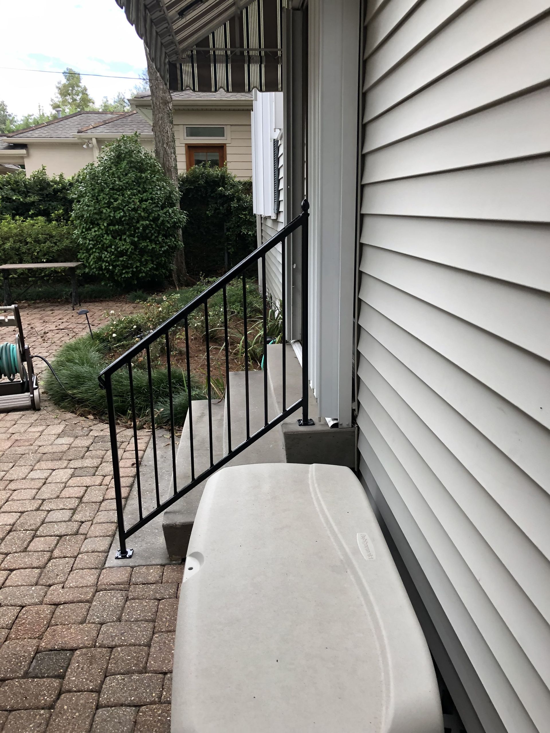 A white cooler sits on the side of a house next to stairs