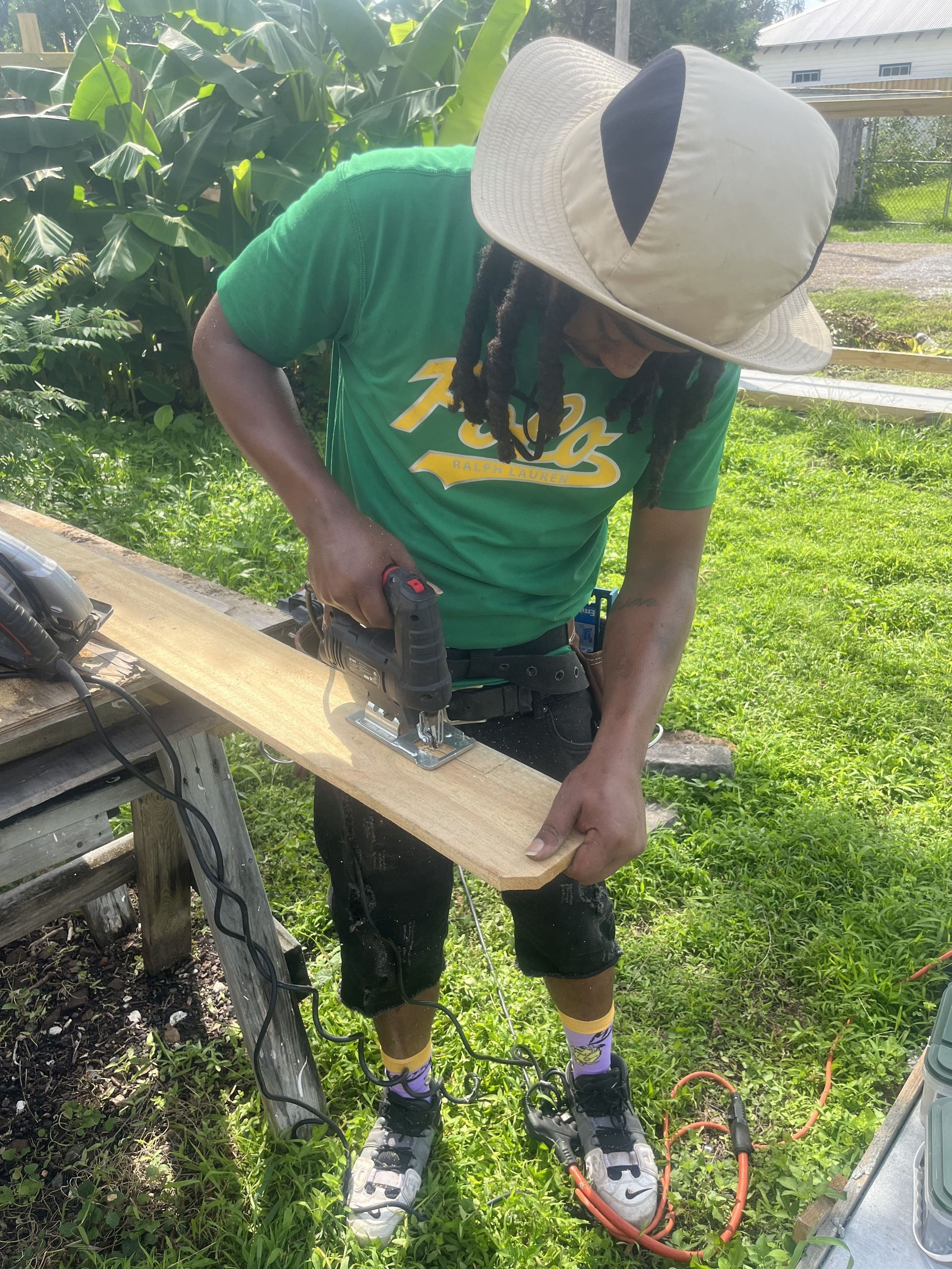 A man in a green shirt is using a jigsaw to cut a piece of wood.