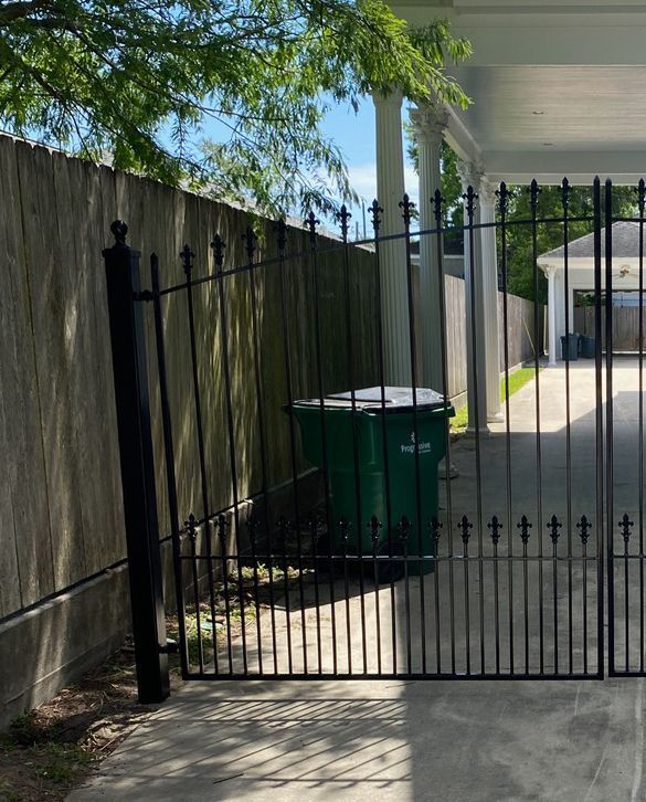 A green trash can is behind a wrought iron gate
