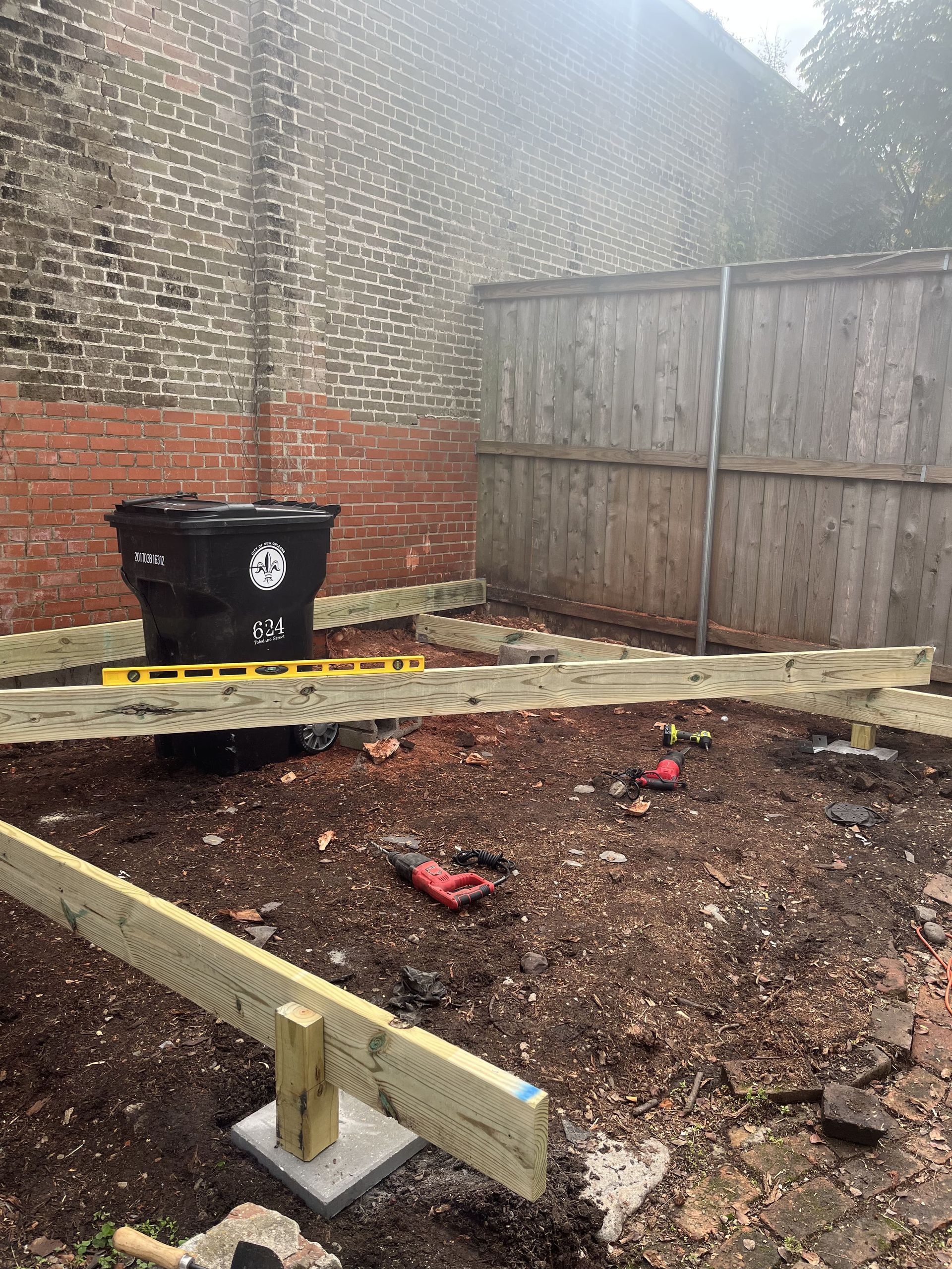A wooden fence is being built in a backyard next to a brick wall.