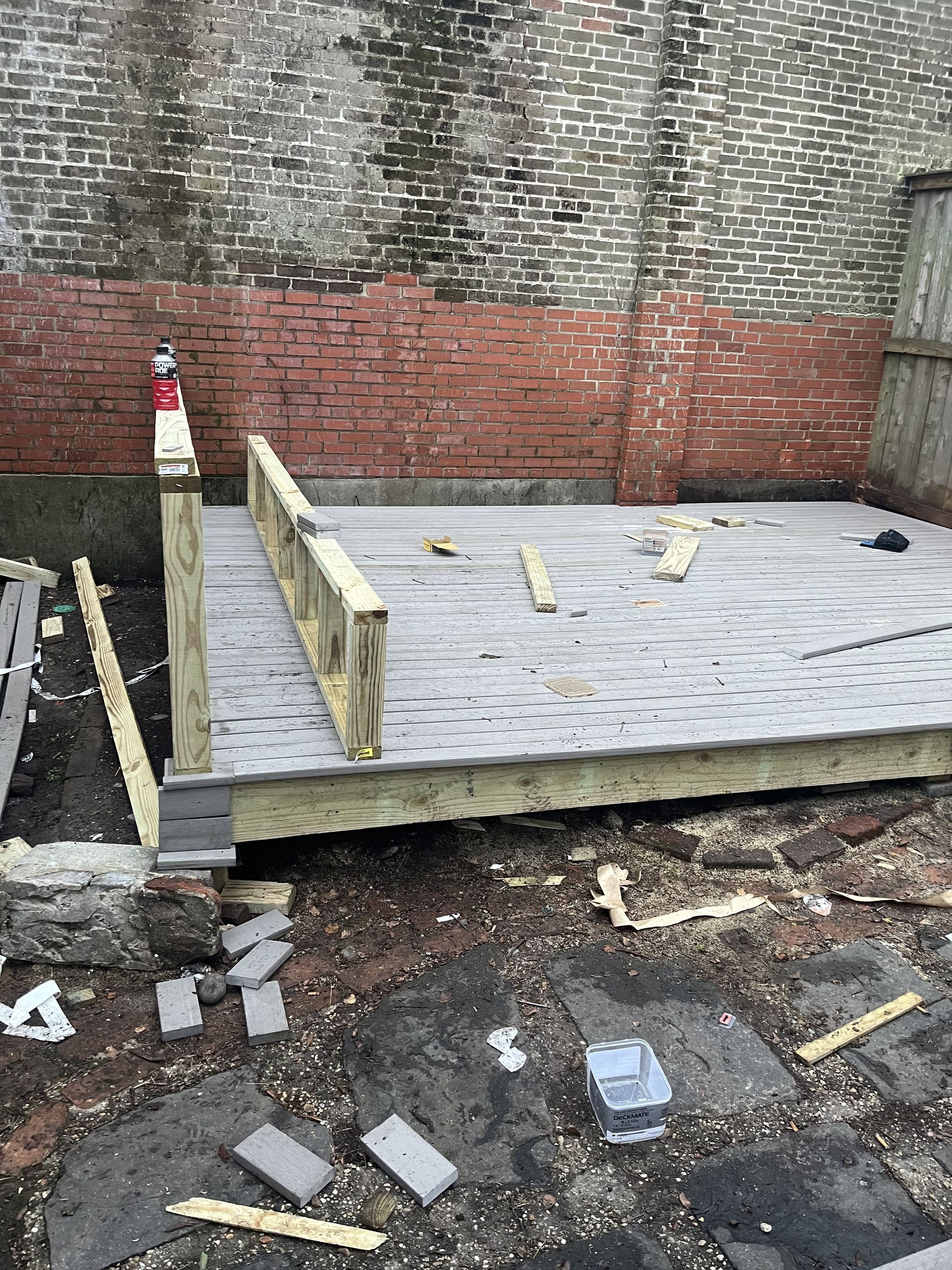 A wooden deck is being built in front of a brick wall.