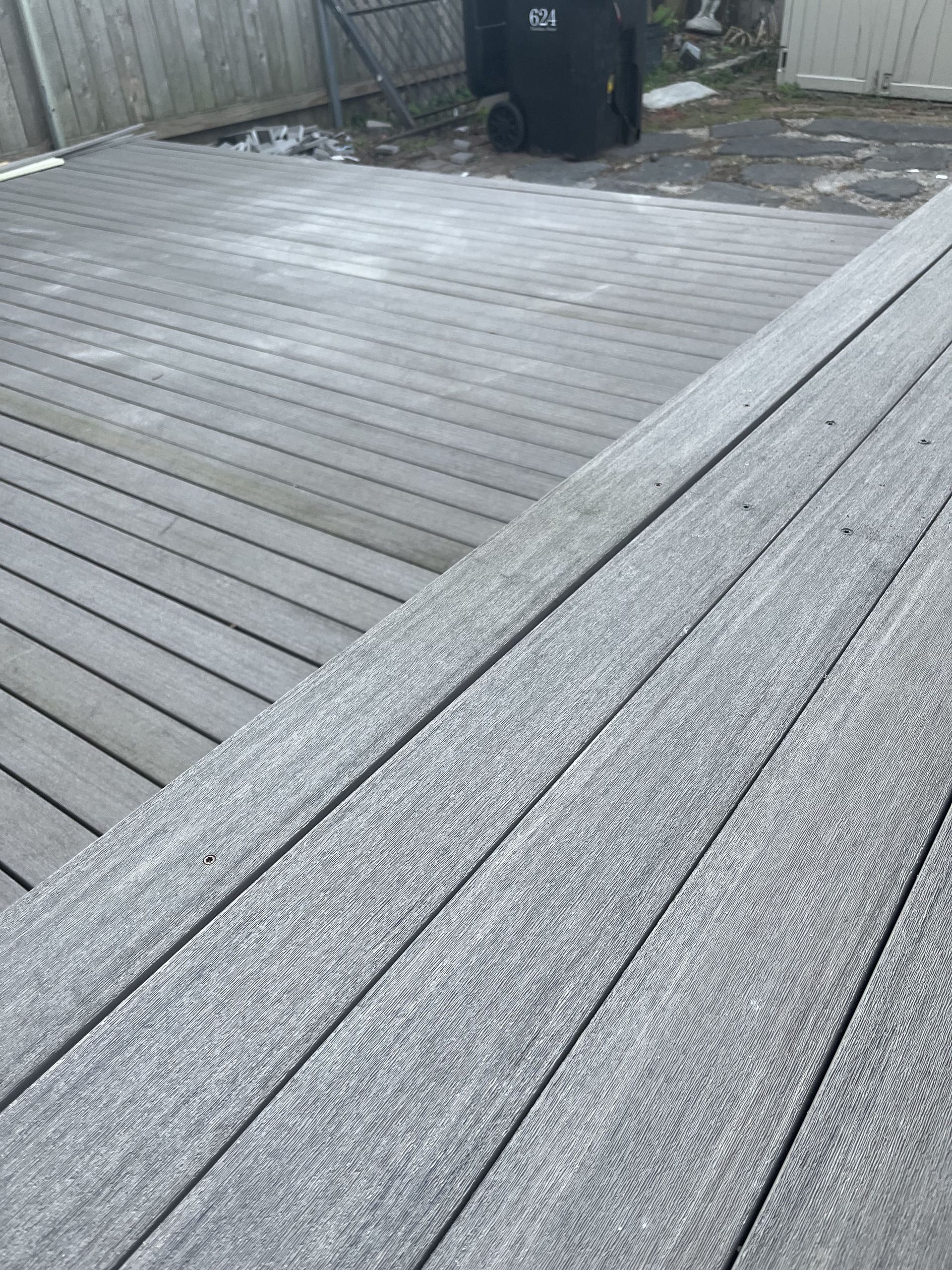 A close up of a wooden deck with a trash can in the background.