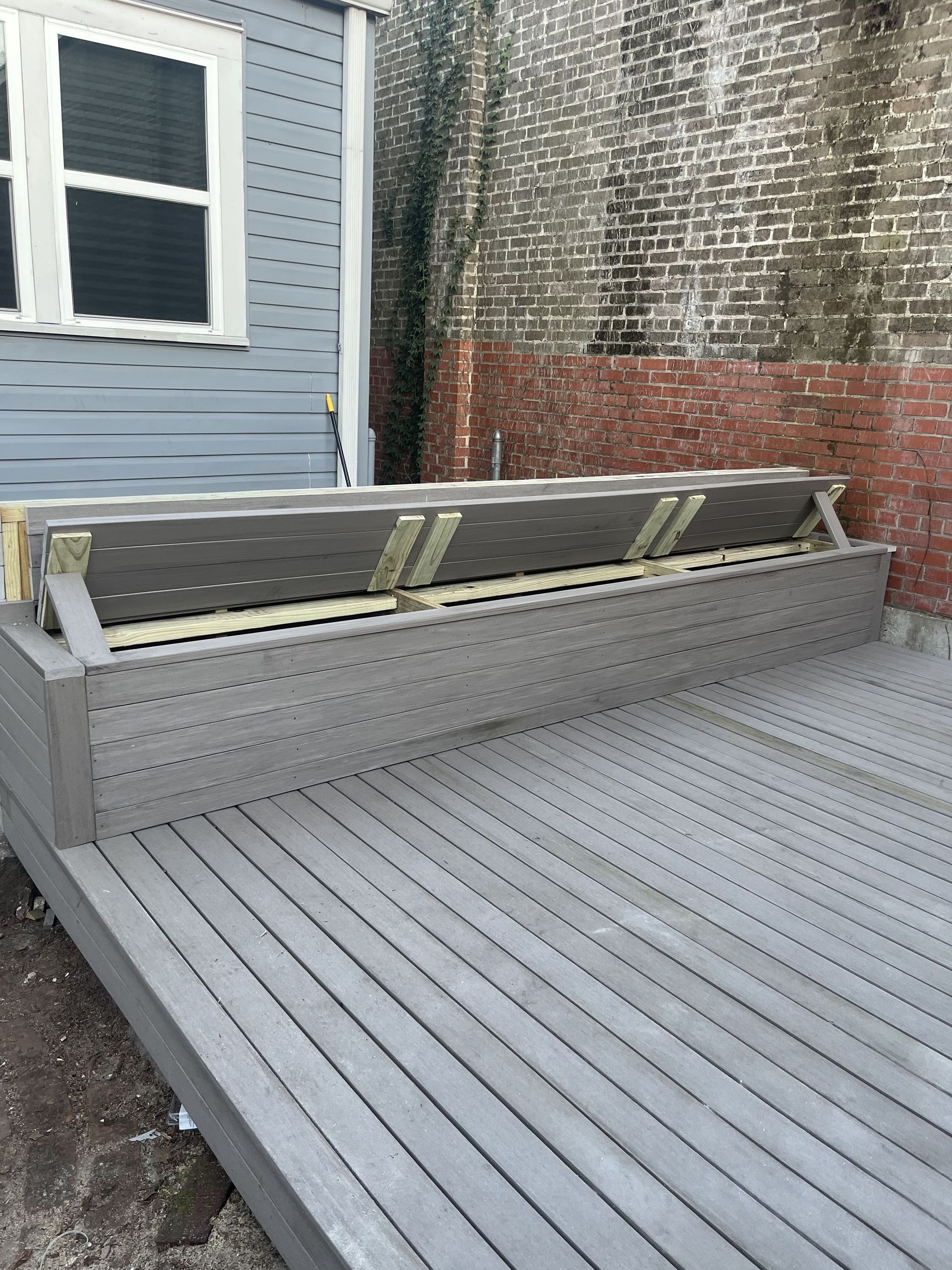 A wooden bench is sitting on a wooden deck in front of a brick building.