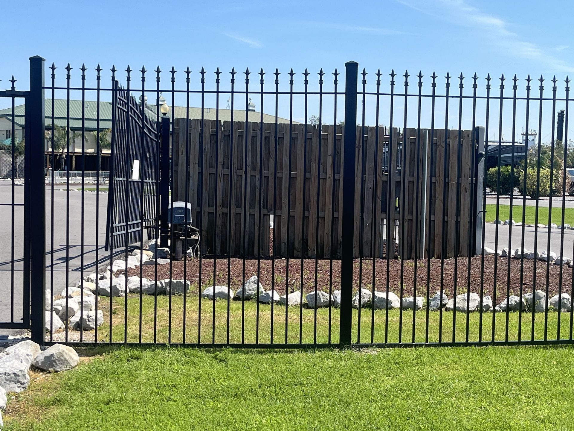 A black metal fence with a wooden fence behind it.