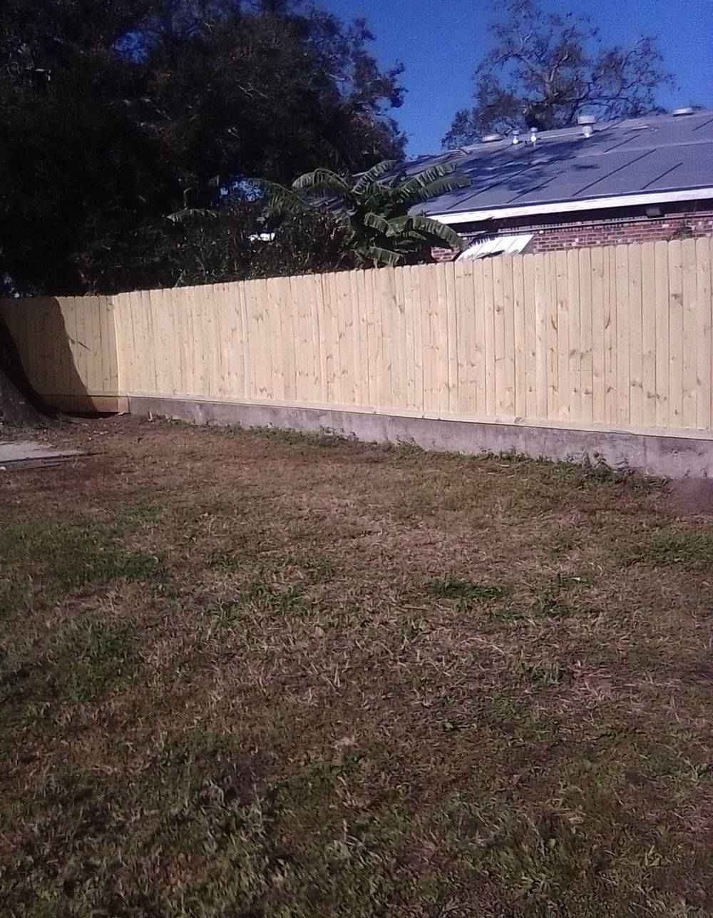 A wooden fence surrounds a grassy yard in front of a house.