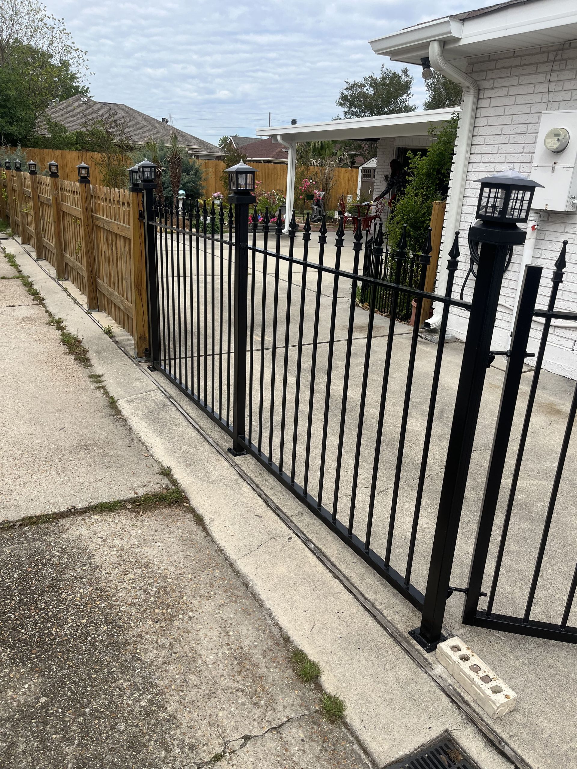 A black wrought iron fence surrounds a driveway in front of a house.