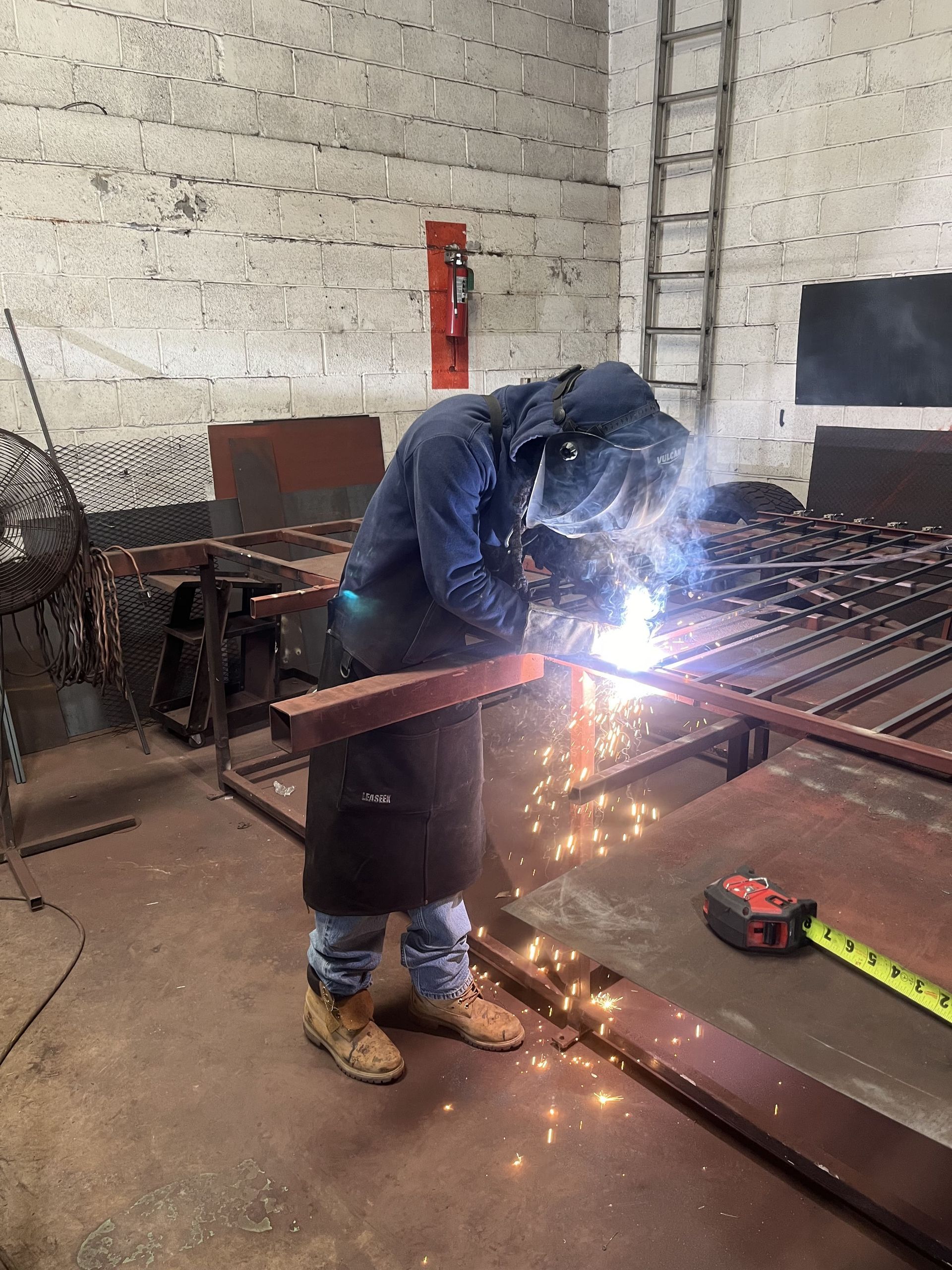 A man is welding a piece of metal in a warehouse.