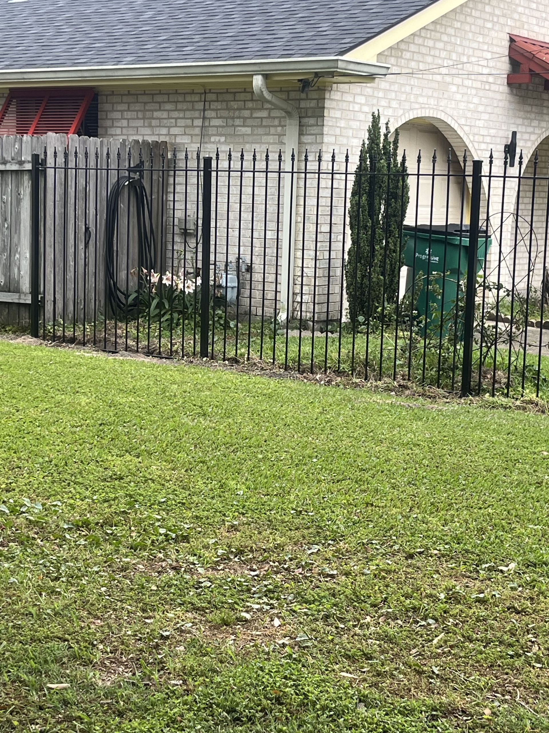 A wrought iron fence surrounds a lush green lawn in front of a house.