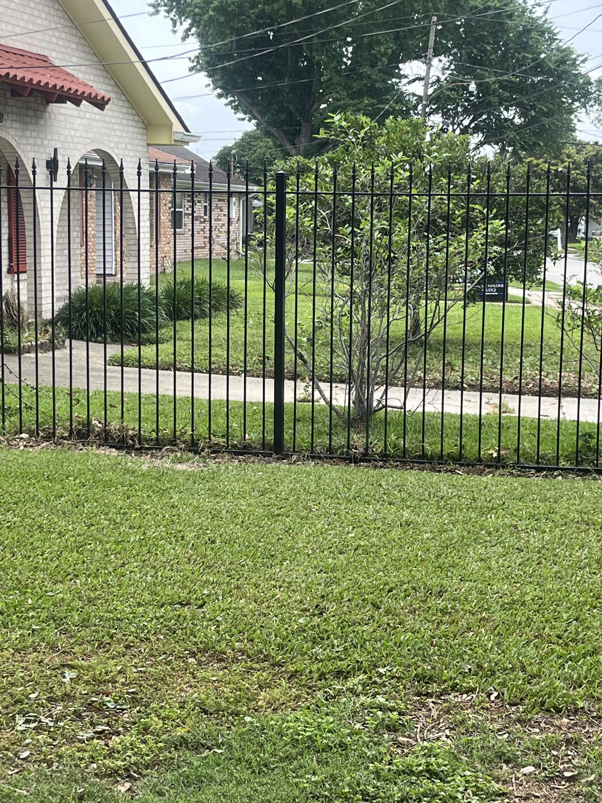 A black metal fence surrounds a lush green lawn in front of a house.