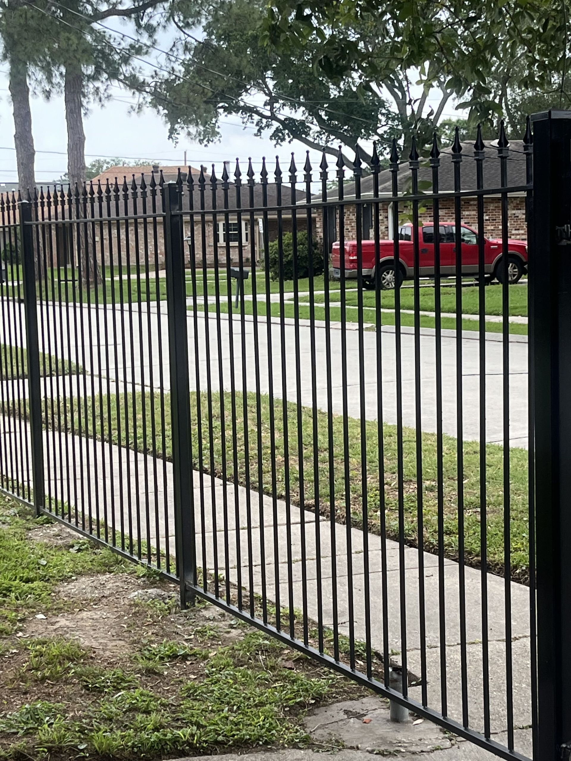 A black wrought iron fence surrounds a sidewalk in a residential neighborhood.