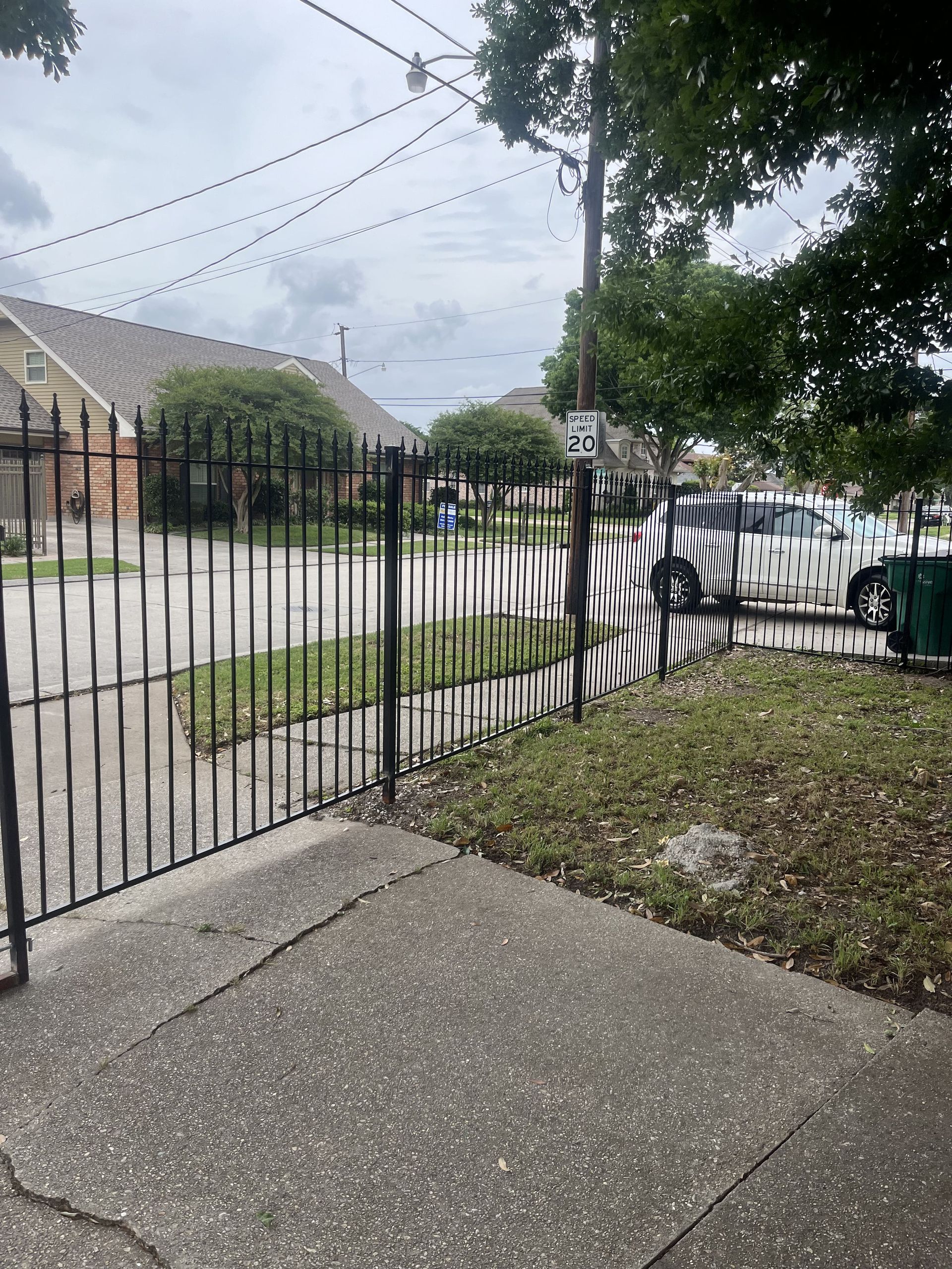 A wrought iron fence surrounds a sidewalk in a residential area.