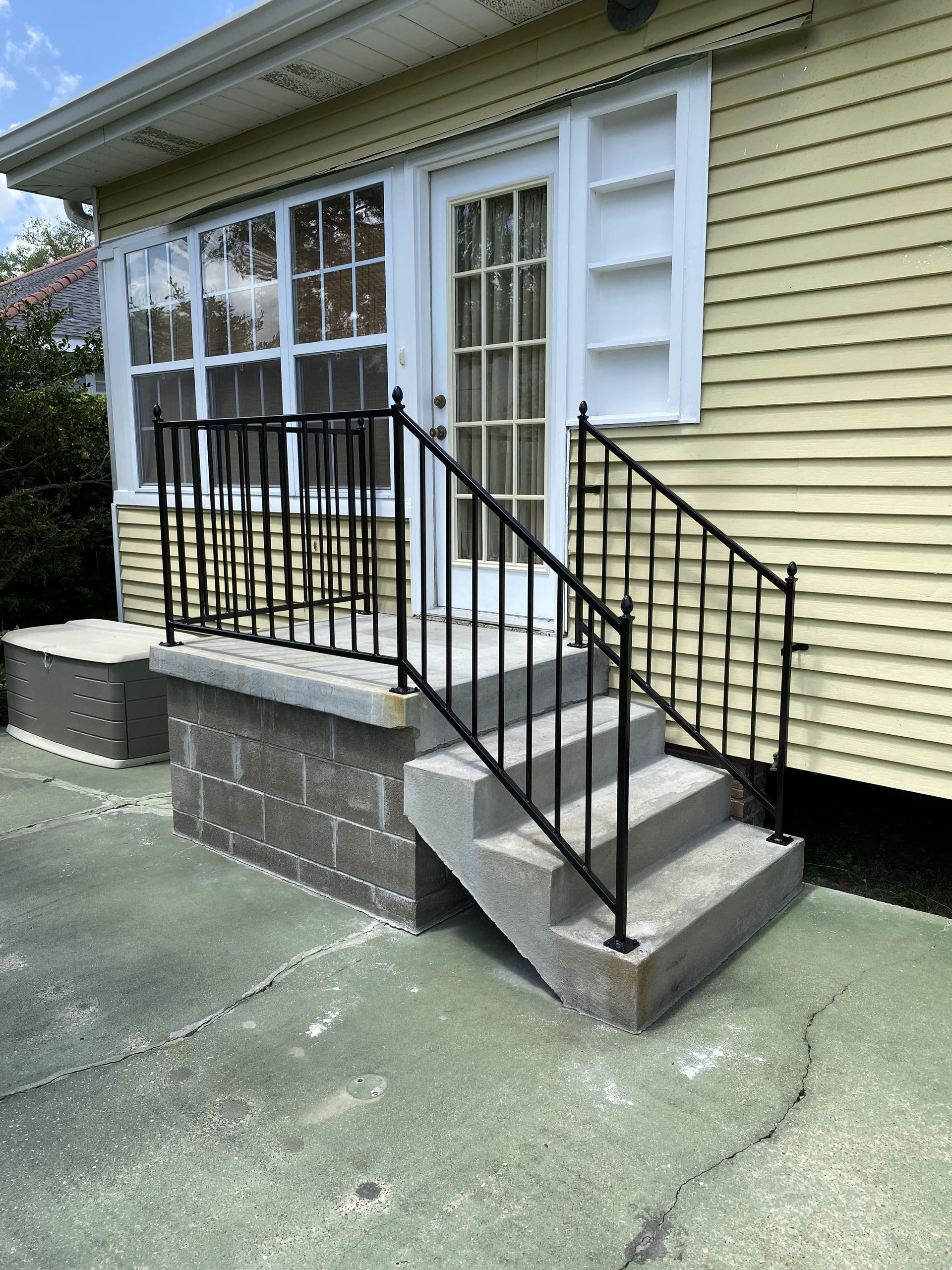 A yellow house with a black railing and stairs