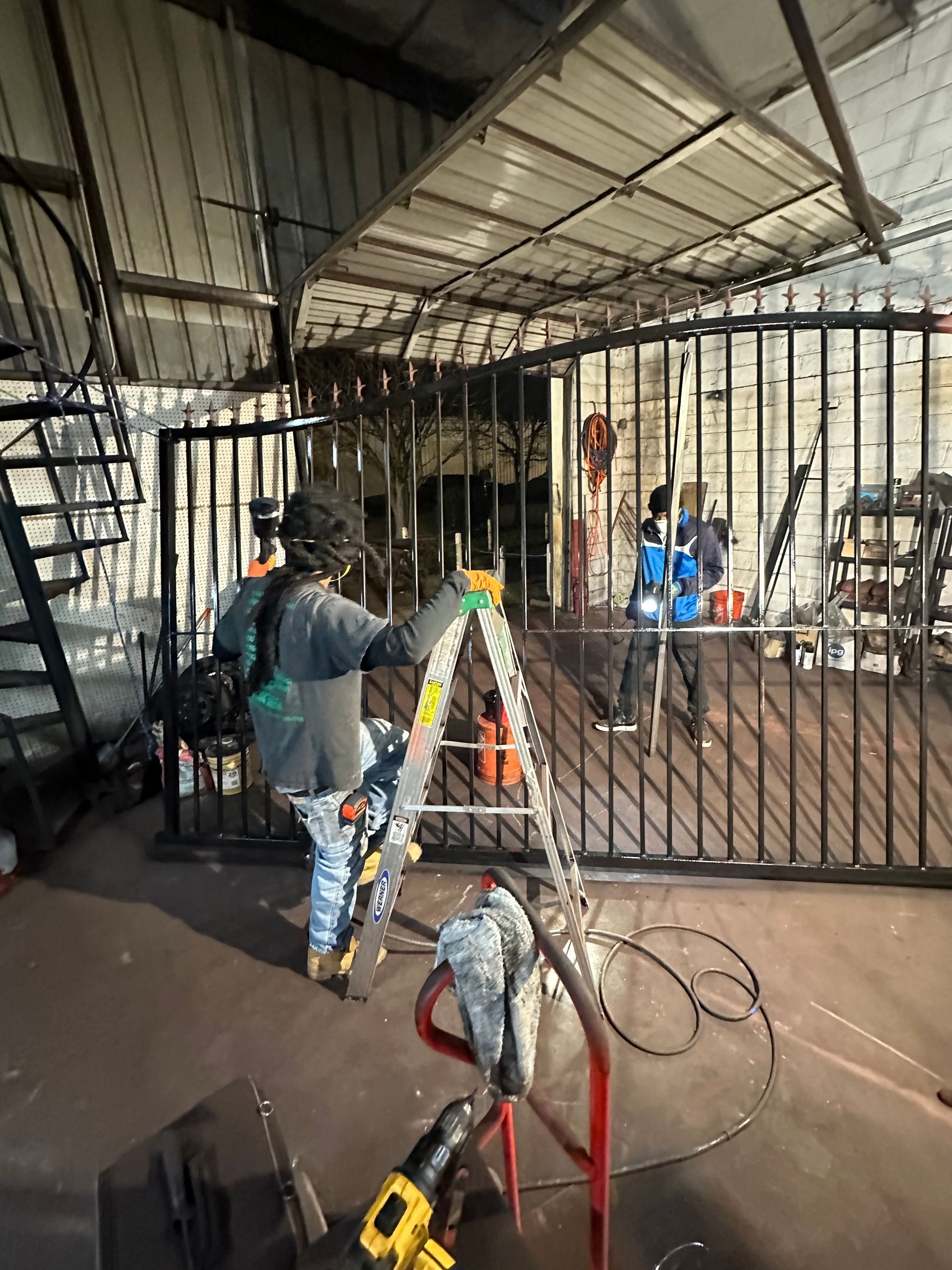 A man is standing on a ladder in front of a metal gate.
