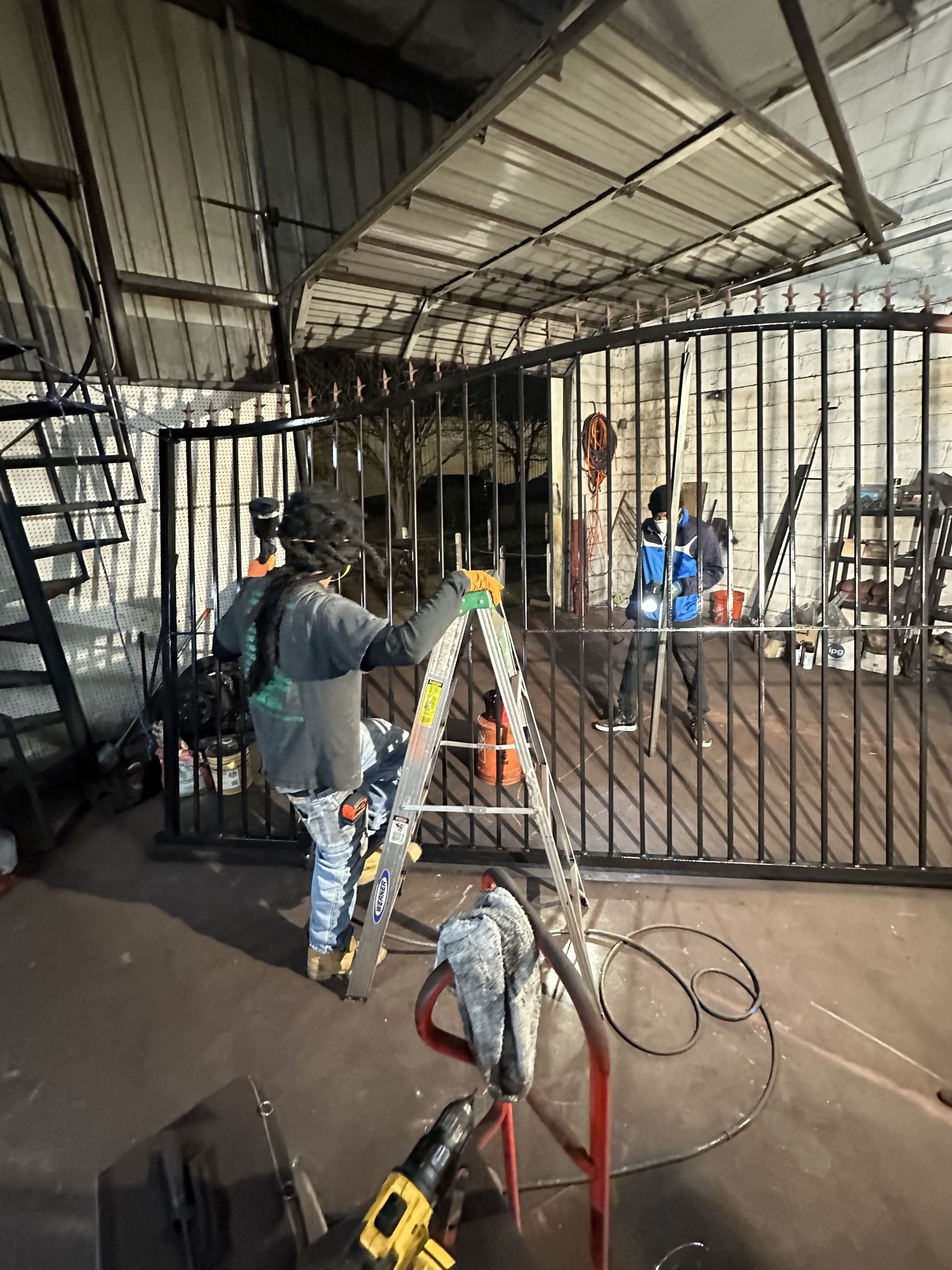 A man is standing on a ladder in front of a metal gate.