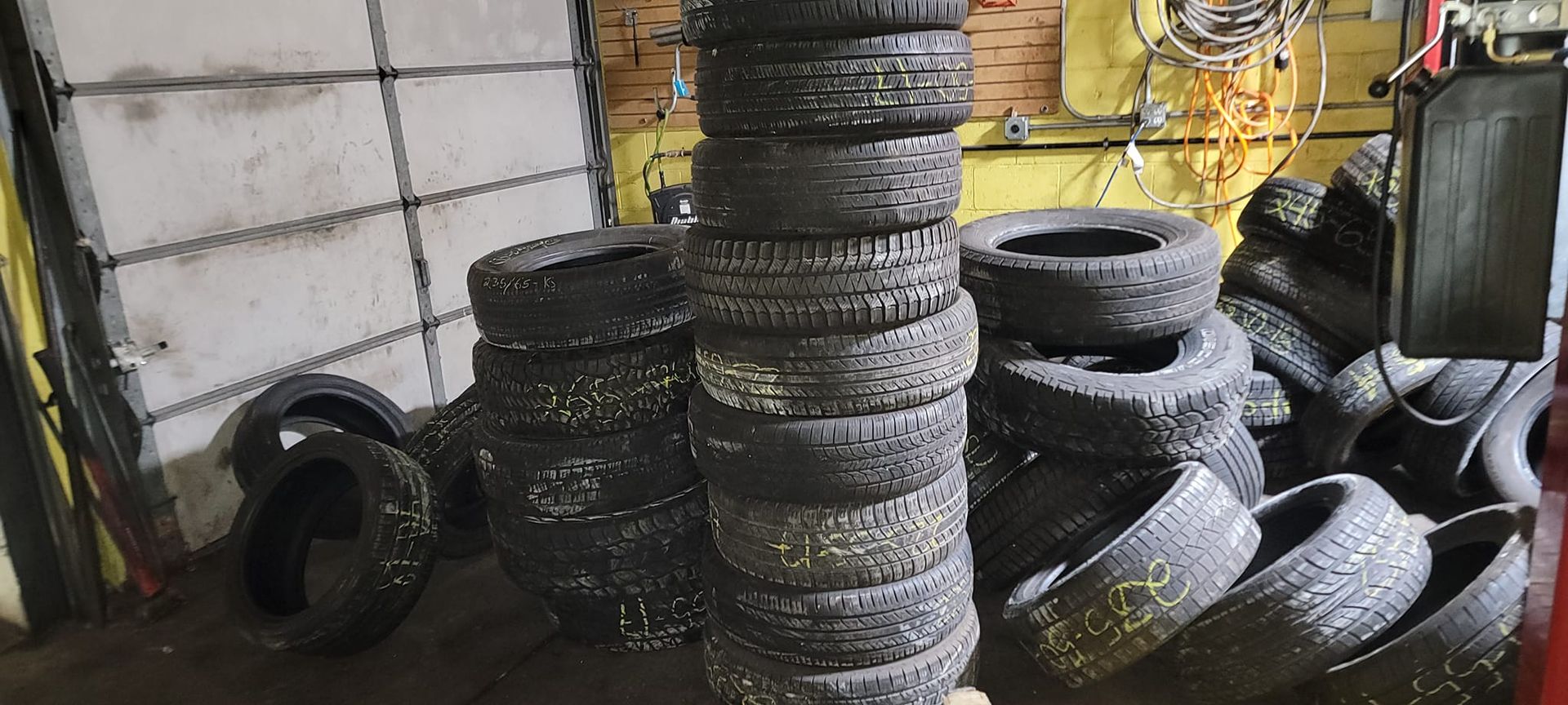 A bunch of tires are stacked on top of each other in a garage.