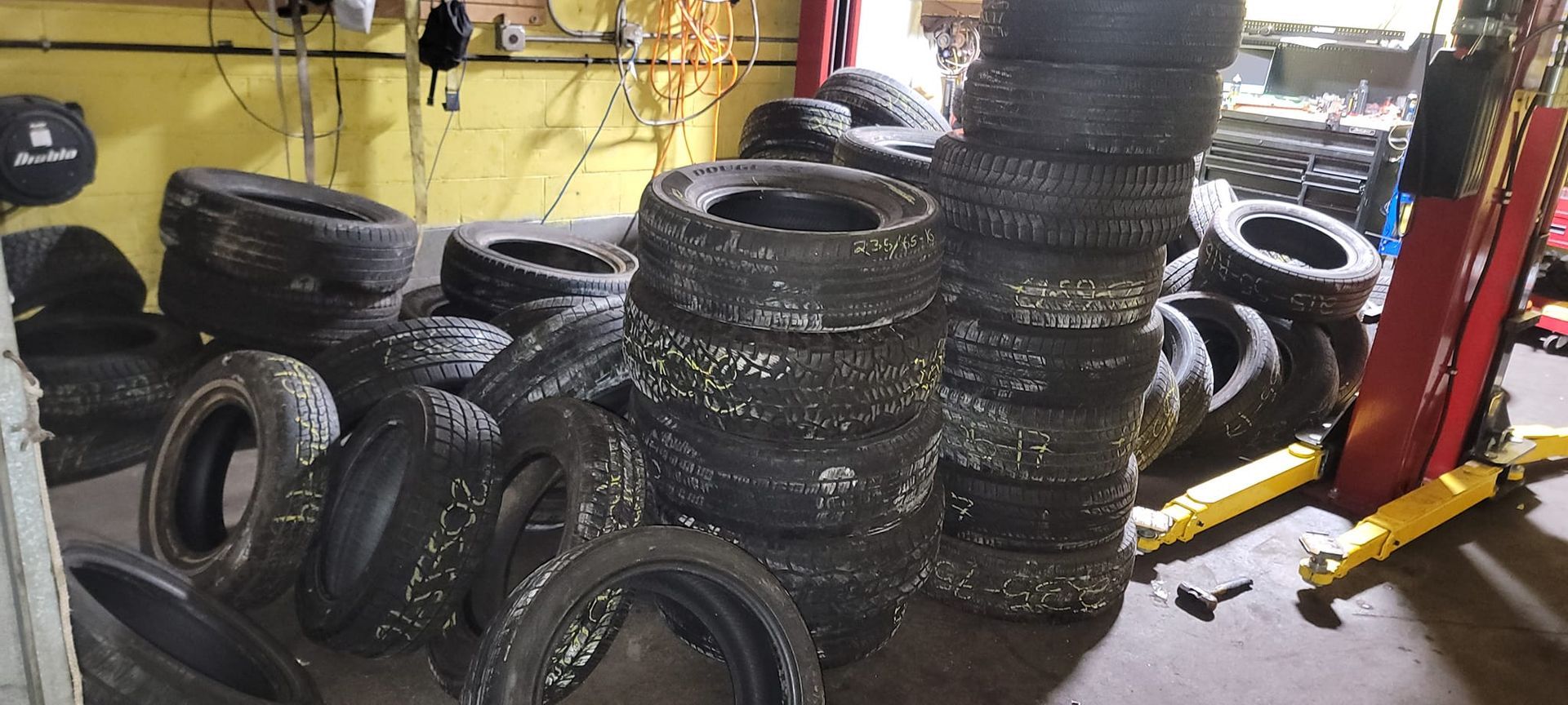 A bunch of tires are stacked on top of each other in a garage.