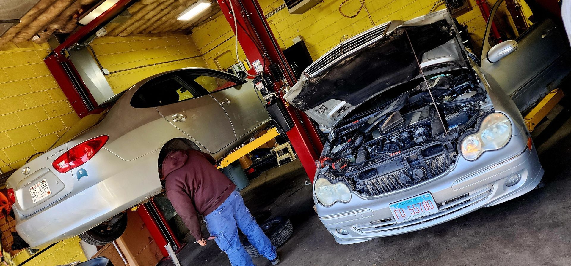 A man is looking under the hood of a car in a garage.