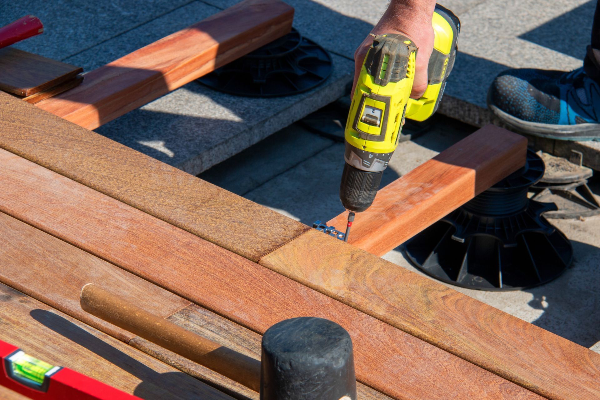 A person is using a drill on a wooden deck.